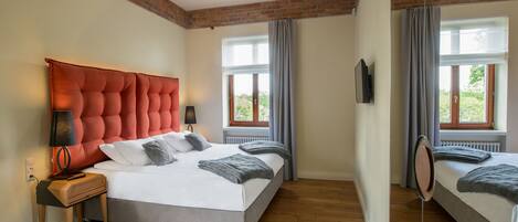 A bedroom with a large bed, a nightstand, a mirror, and a window with curtains.