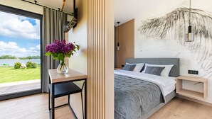 Ein modernes Schlafzimmer mit großem Fenster, einem Nachttisch mit Blumenvase, einem Bett mit grauer Decke und einer Wand mit strukturierter Gestaltung.