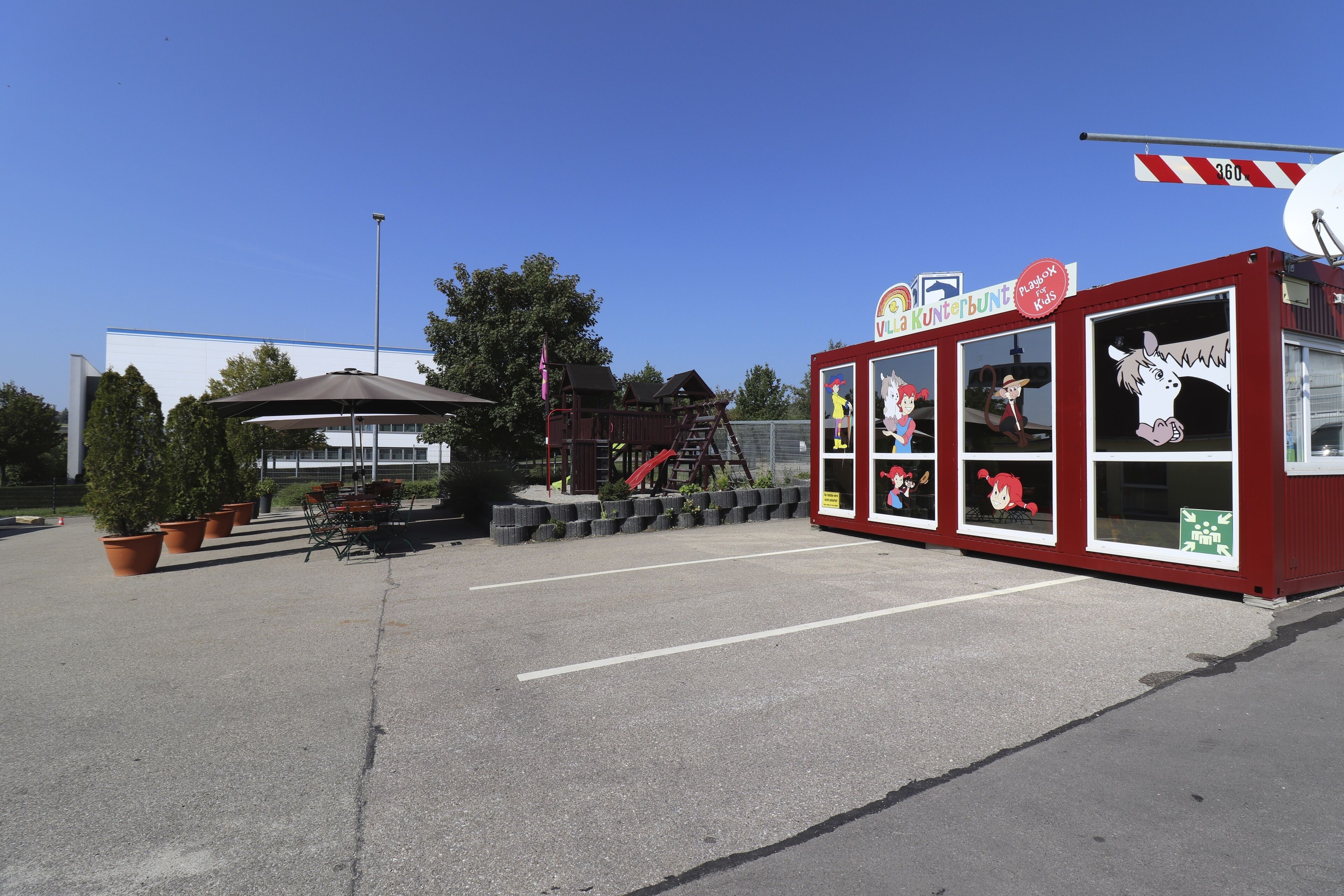 A red building with cartoon characters on the windows, a playground, and potted plants.