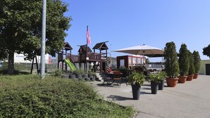 A playground with a slide and climbing structures, surrounded by potted plants and outdoor seating. - IQ Hotel (Langenau)