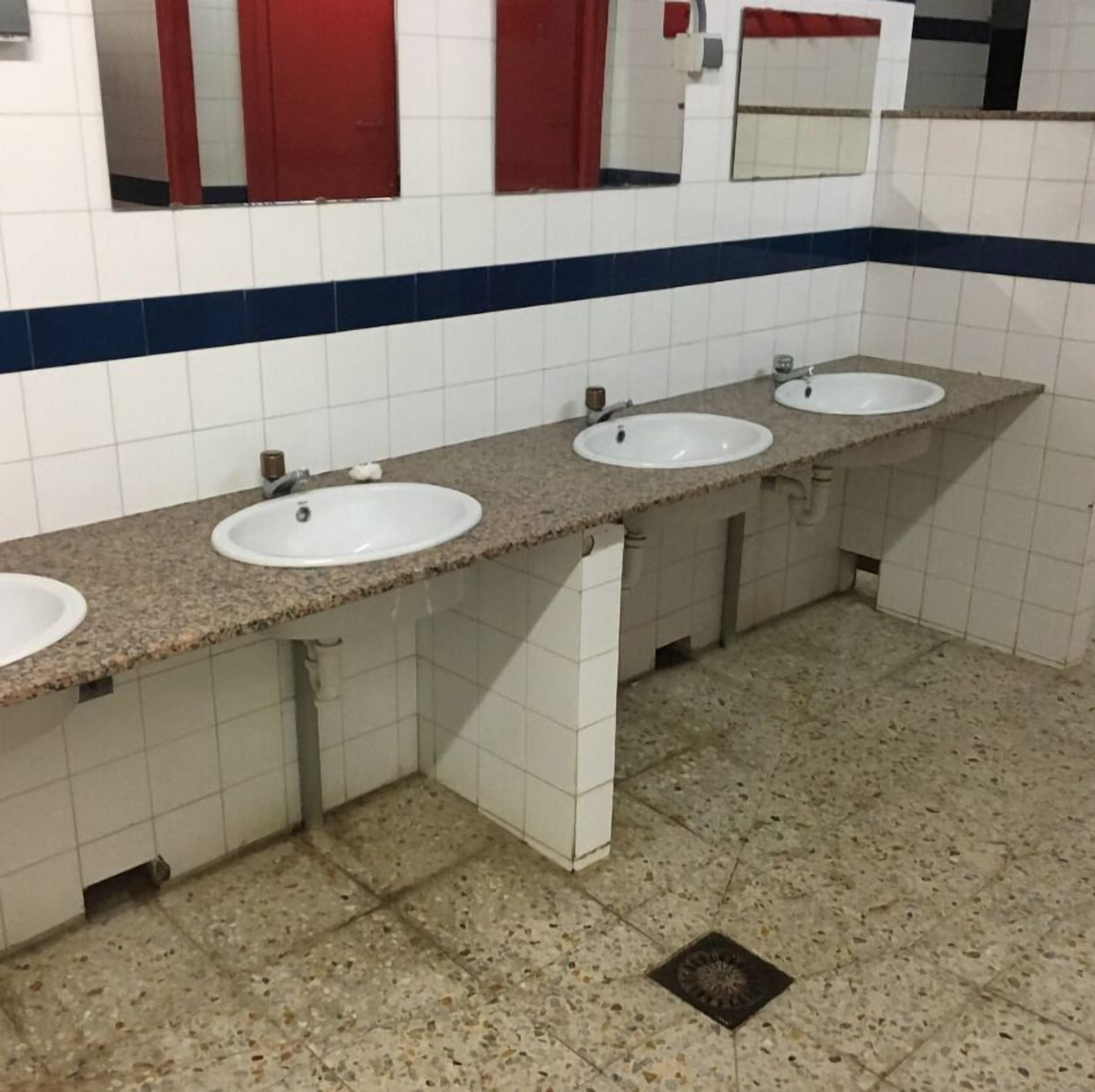 A public restroom with three sinks, white tiled walls, and a blue stripe.