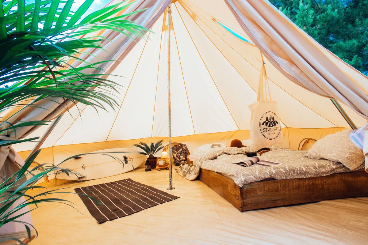 A cozy tent with a bed, a small table, and a potted plant.