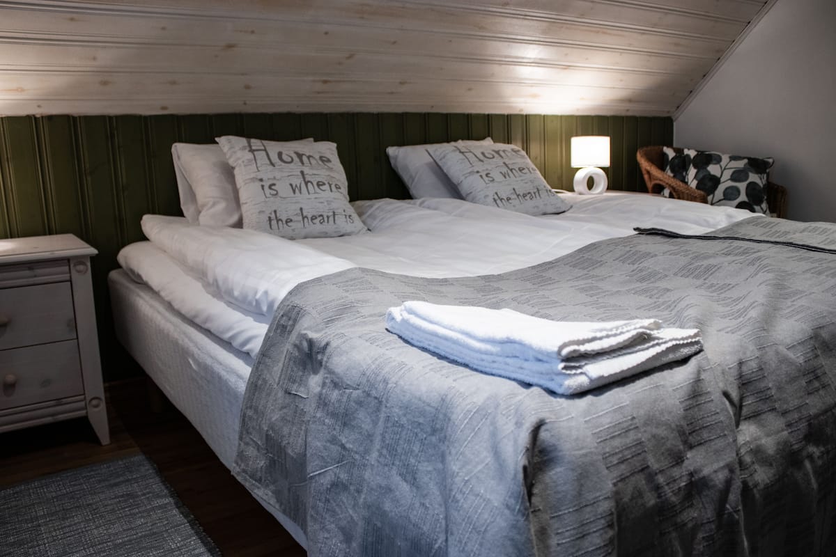 A bedroom with a bed, pillows with text, a nightstand, a lamp, and a chair.