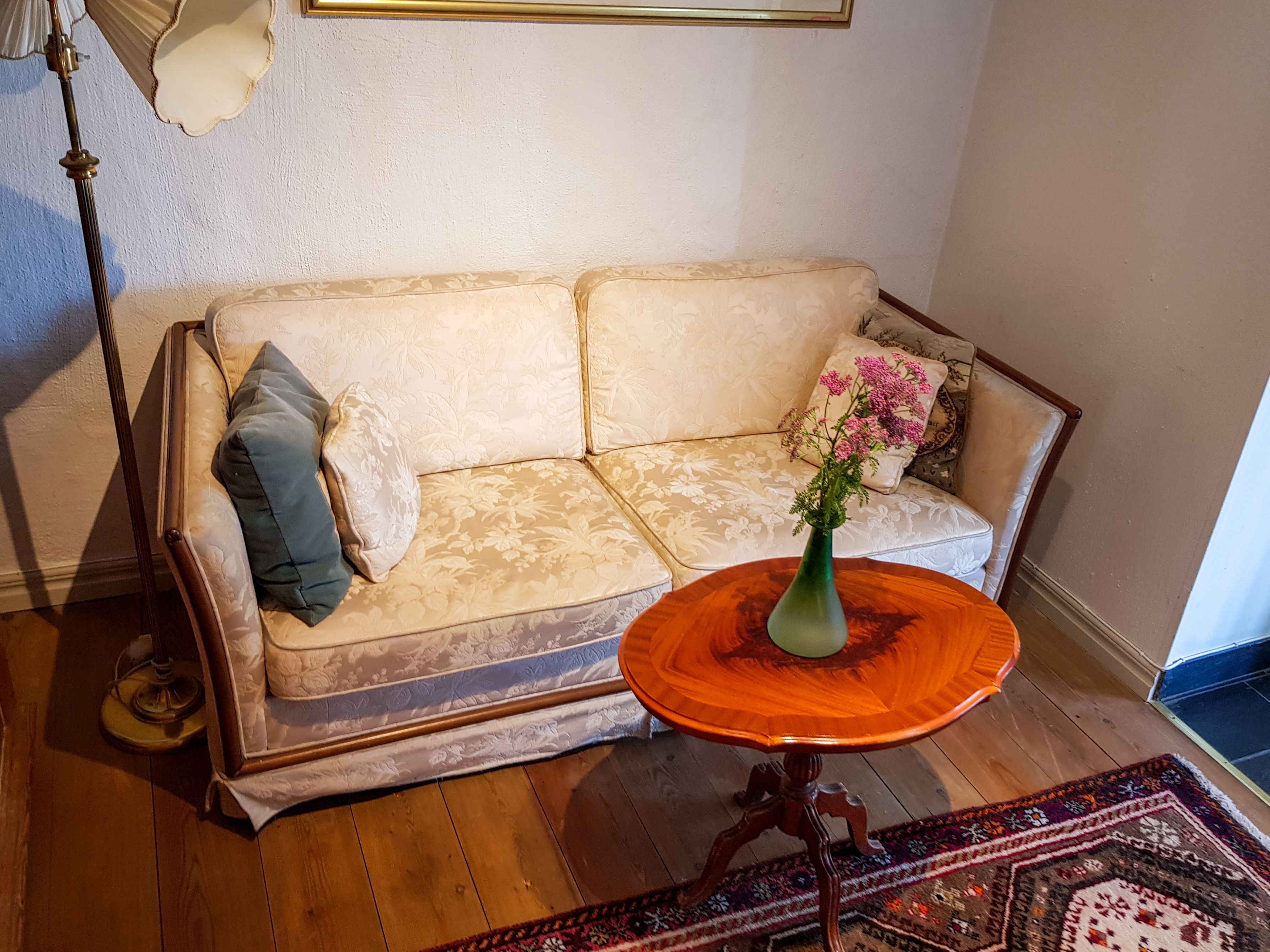Un salón con sofá, una mesa de centro redonda de madera, alfombra estampada y una lámpara de pie.