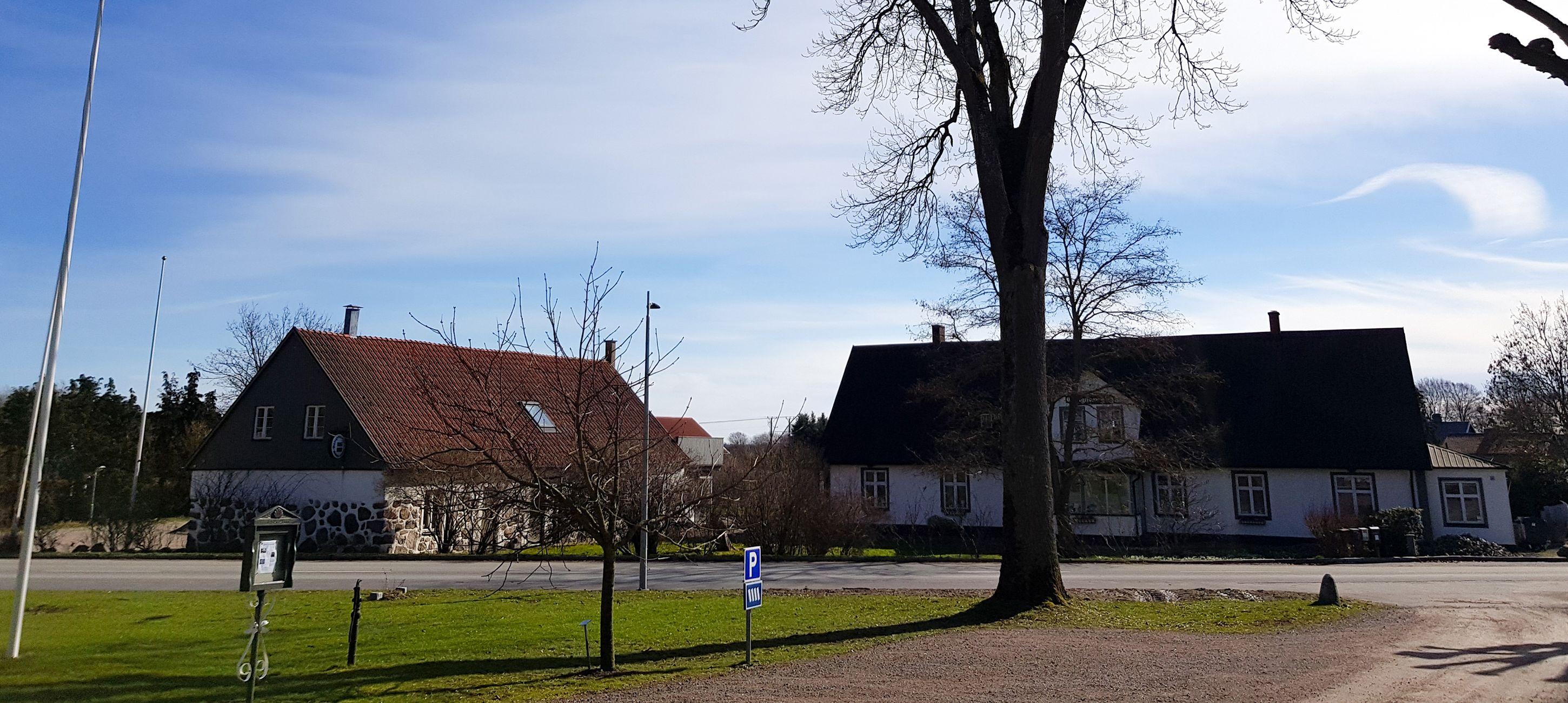 A rural street with two houses, one with a stone facade and the other with a white exterior.