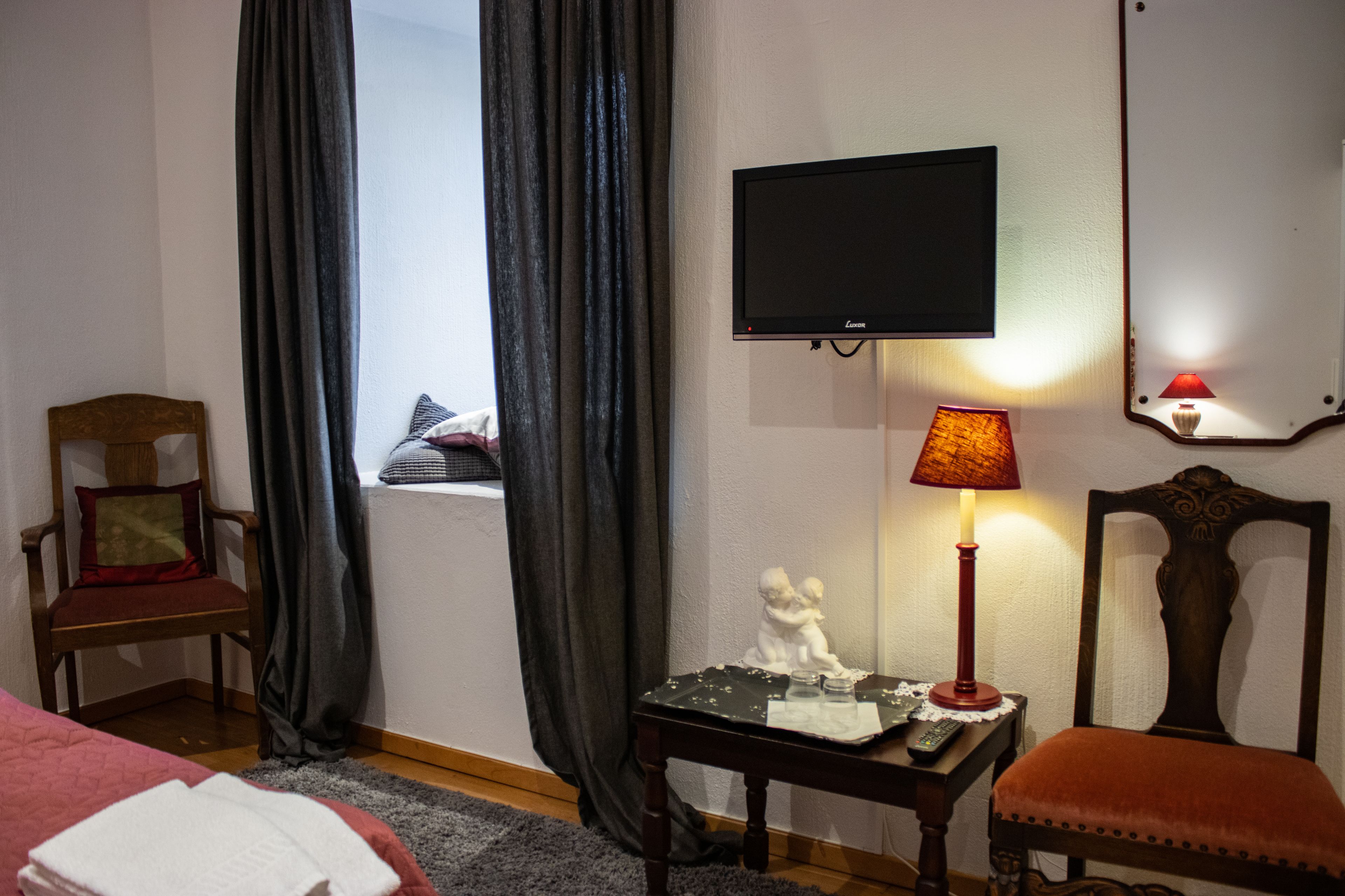 A hotel room with a bed, a chair, a table with a lamp, a television, and a window with curtains.