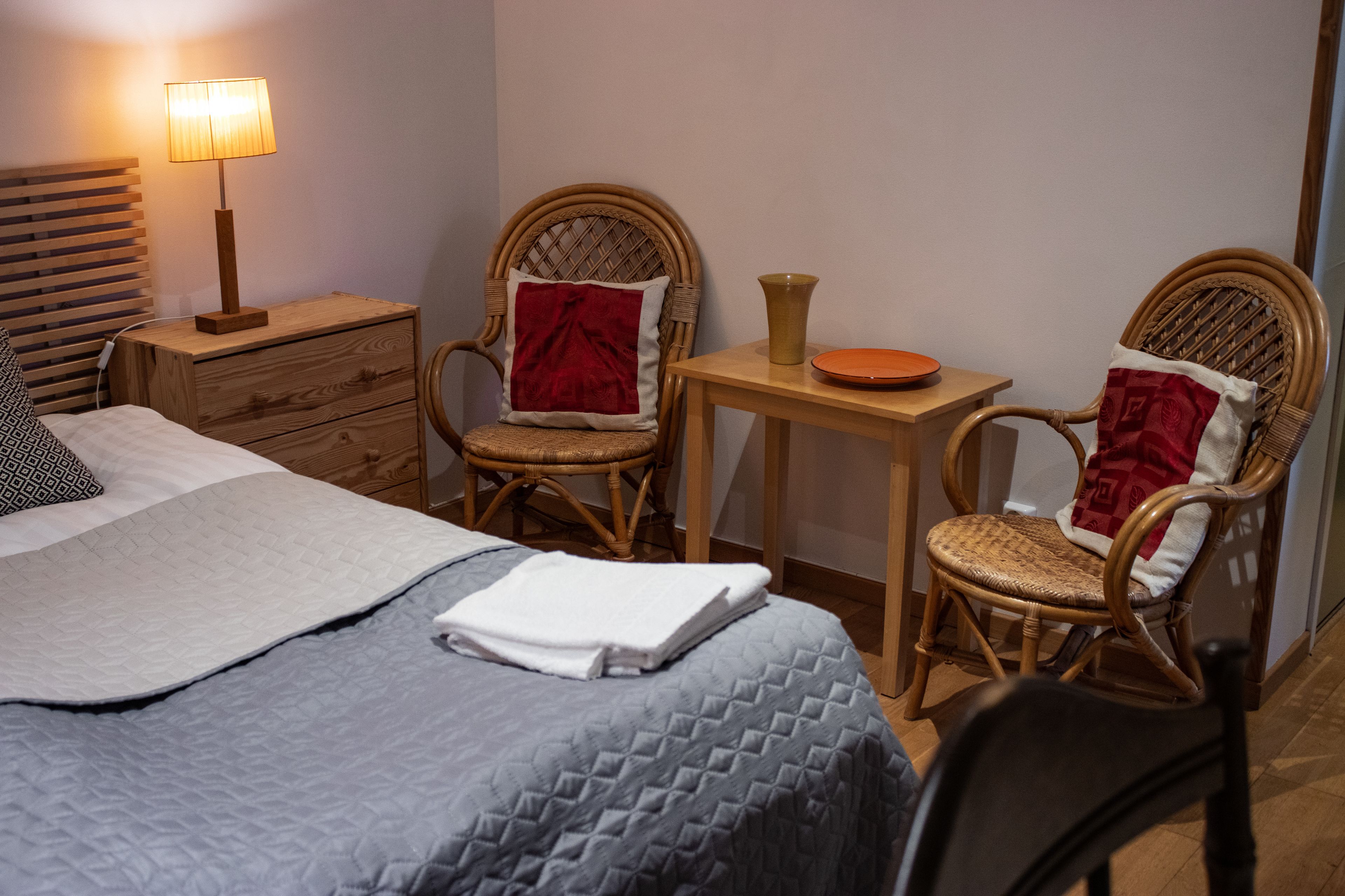 Une chambre à coucher bien rangée, avec un lit, deux fauteuils en osier, une petite table en bois, une lampe et une table de chevet.