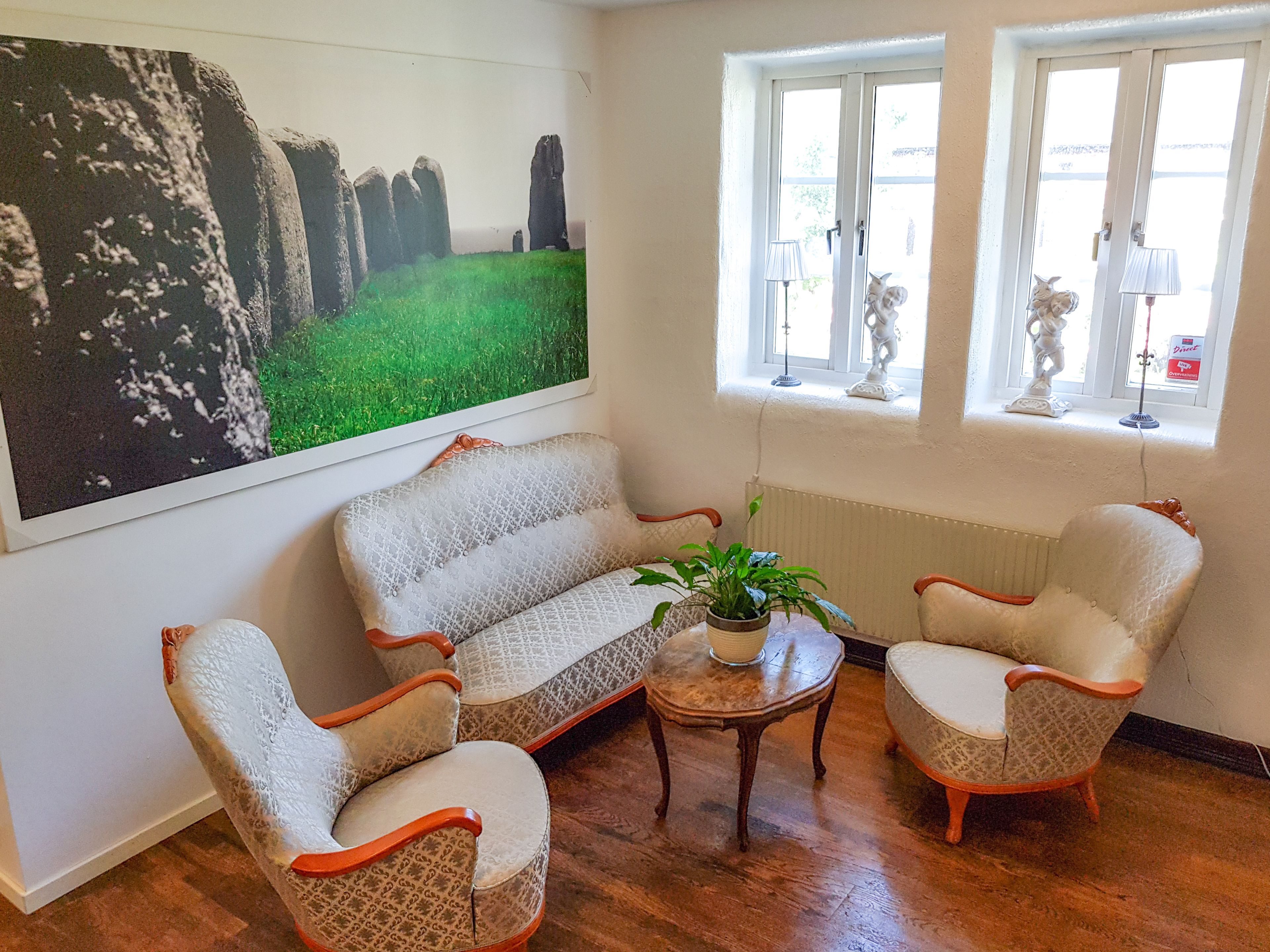 Un salon comprenant un canapé, deux fauteuils, une petite table avec une plante et un grand tableau représentant Stonehenge.