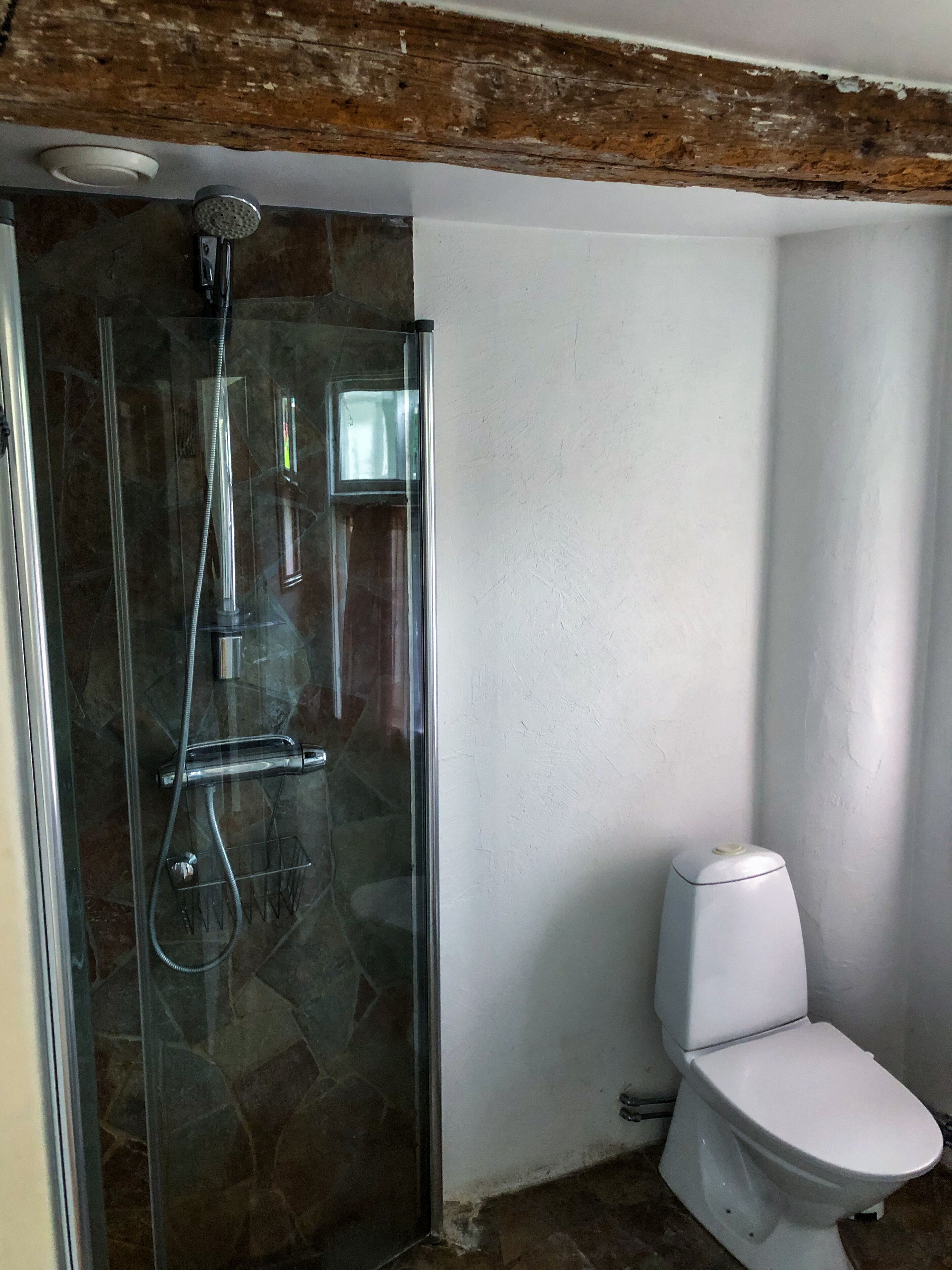 Une salle de bain avec une douche à parois de verre, des toilettes blanches et un sol carrelé en pierre.