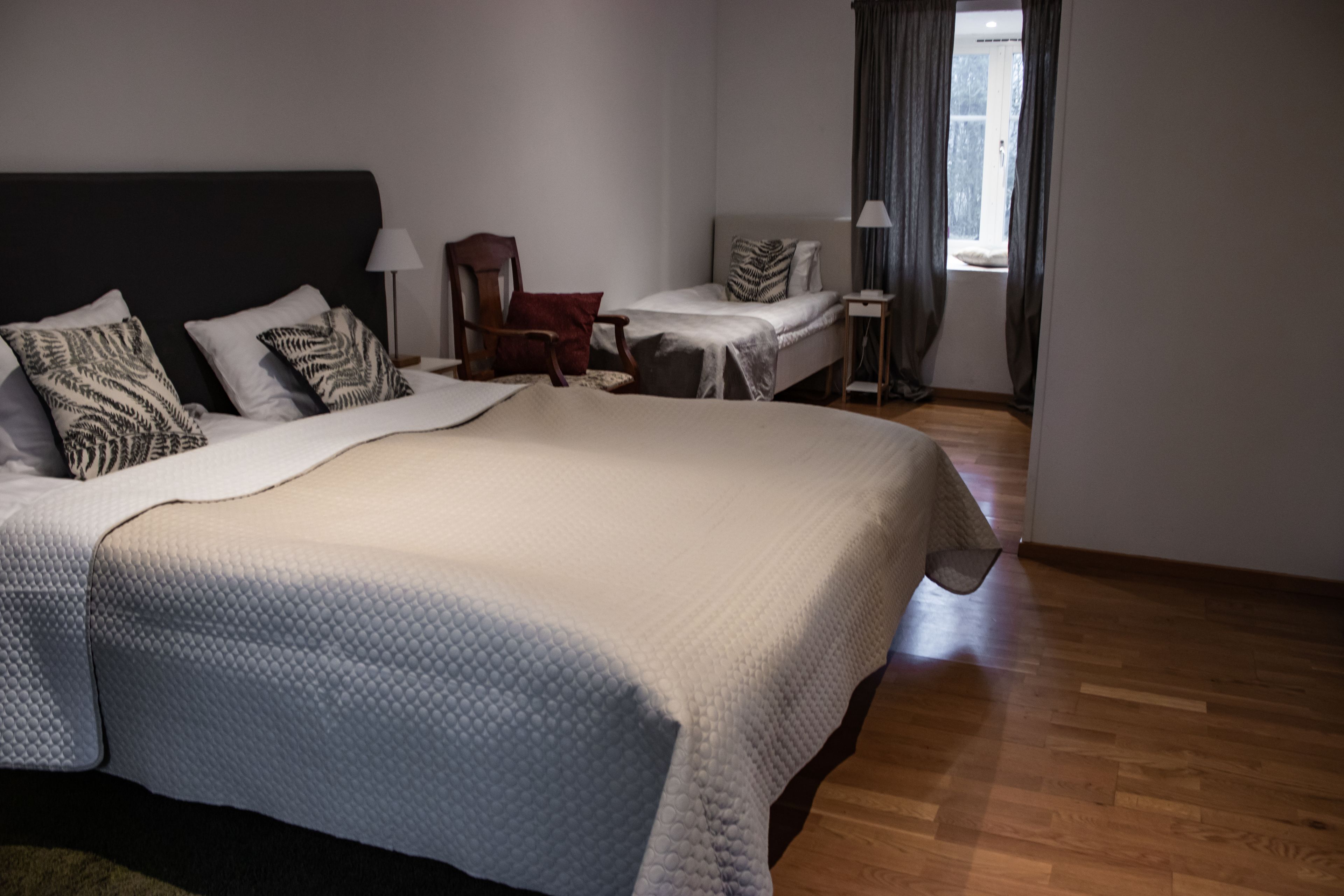 Una habitación de hotel con una cama grande, una silla, una mesita y un ventanal con cortinas.