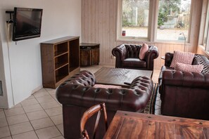 A living room with a wooden coffee table, leather sofas, a wooden cabinet, and a television mounted on the wall. - Stora Herrestad Bed & Breakfast (Ystad)