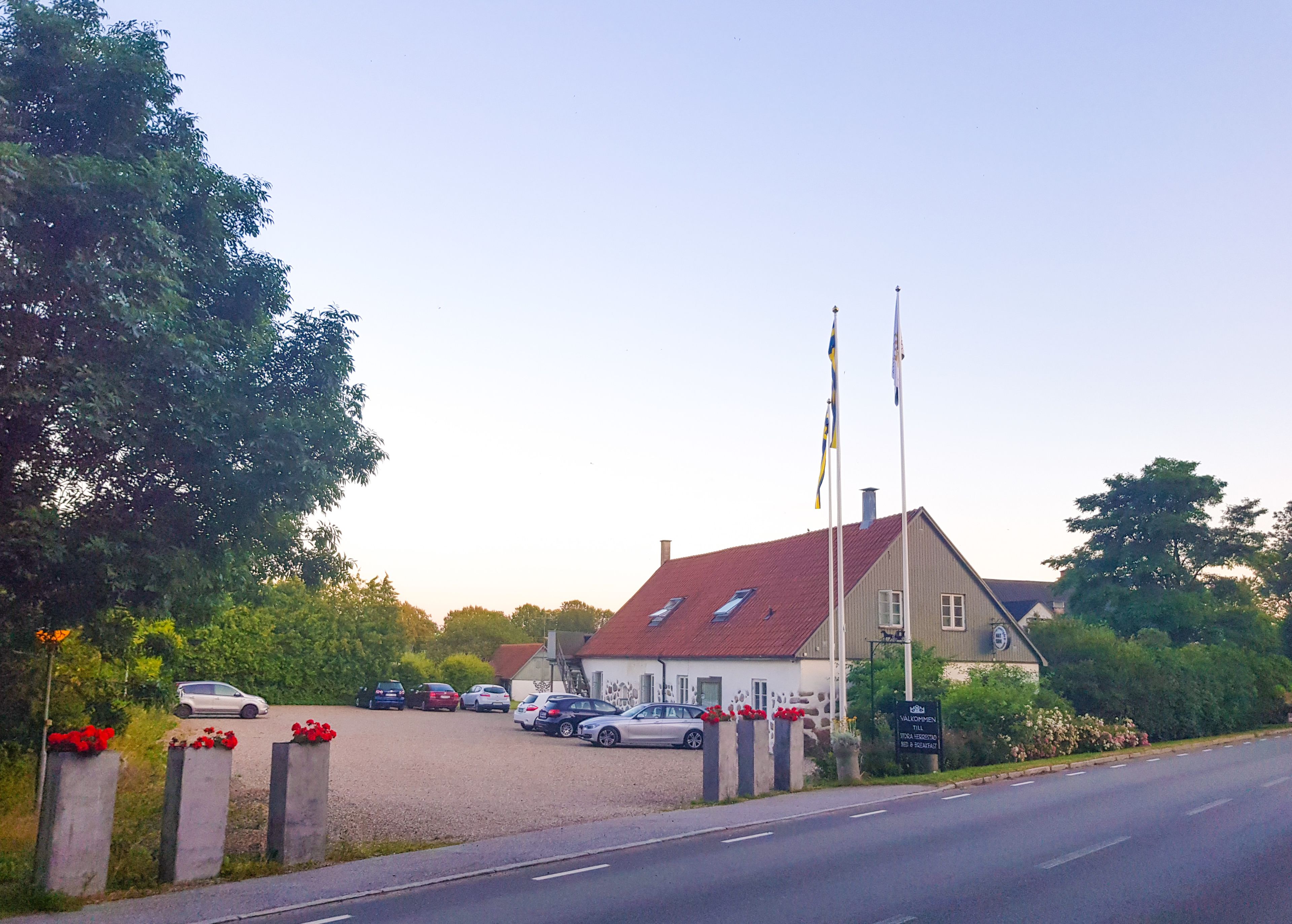 A building with a red roof, multiple flags, and a parking lot with several cars.