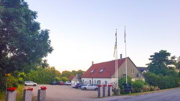 A building with a red roof, multiple flags, and a parking lot with several cars.