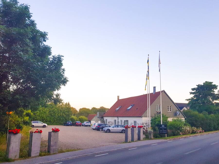 A building with a red roof, multiple flags, and a parking lot with several cars.