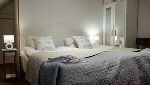 A neatly made bed with a quilted blanket and two pillows with text. There is a bedside table with a lamp and a small shelf. - Stora Herrestad Bed & Breakfast (Ystad)