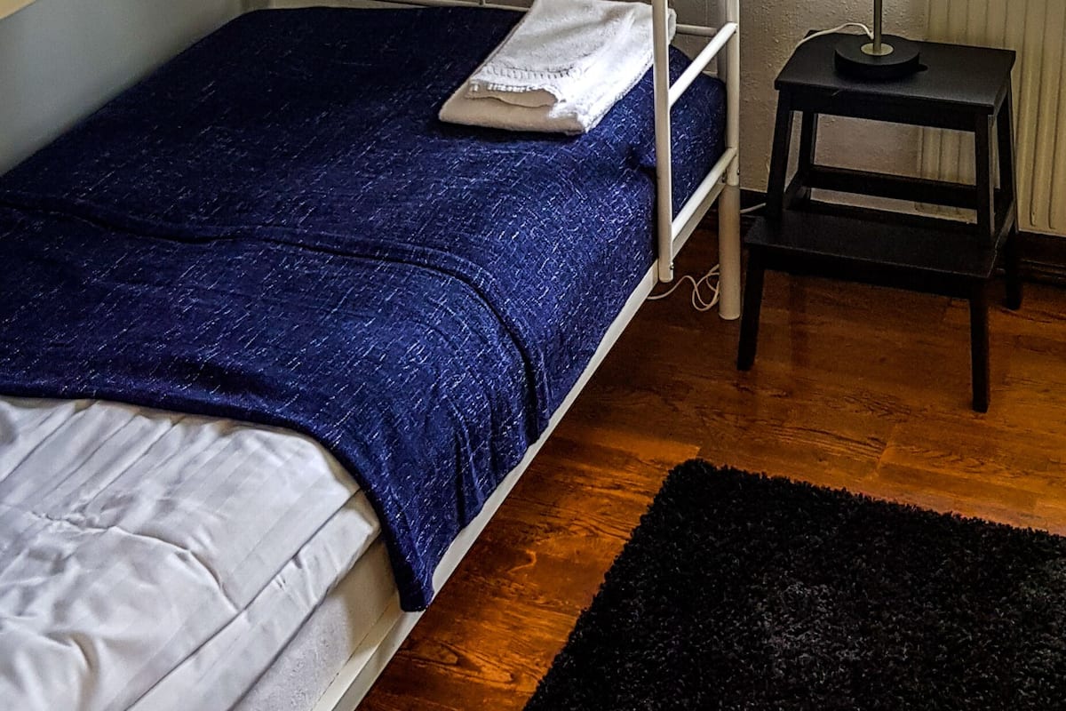 A bunk bed with white and blue bedding, a small black desk with a lamp, and a black rug on a wooden floor.