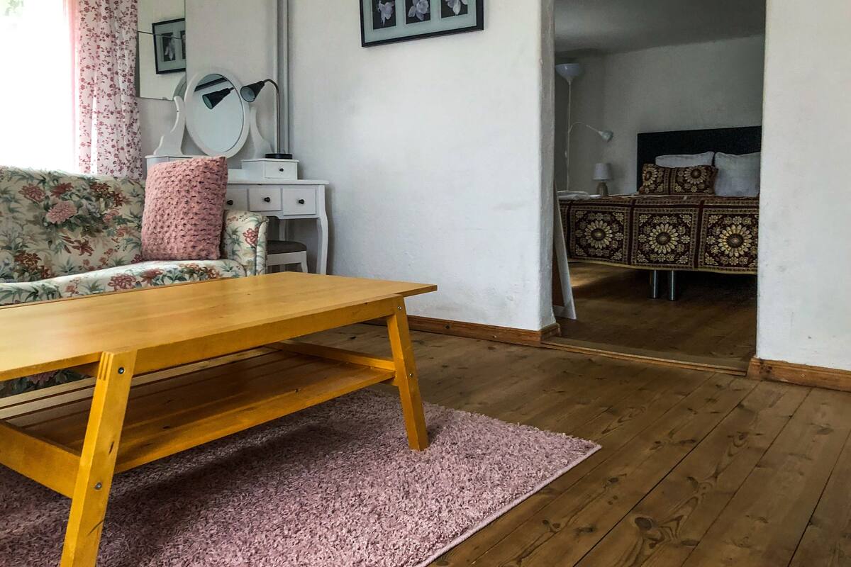 A room with a wooden table, a floral sofa, a white dresser, and a patterned bed.