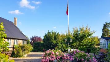 Jardín residencial con asta de bandera, un sendero de grava y diversas plantas florecientes.