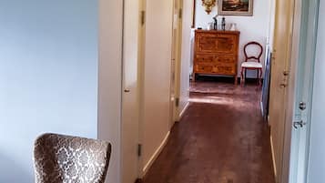 A hallway with wooden flooring, a patterned armchair, and a ceiling with ornate metalwork.