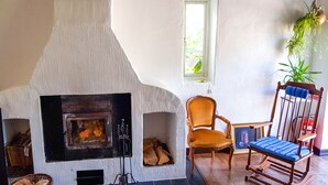 A cozy room with a fireplace, a wooden rocking chair, and a chair with a blue cushion. - Stora Herrestad Bed & Breakfast (Ystad)