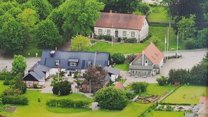 A large, two-story house with a sloped roof, surrounded by well-maintained lawns and trees. - Stora Herrestad Bed & Breakfast (Ystad)