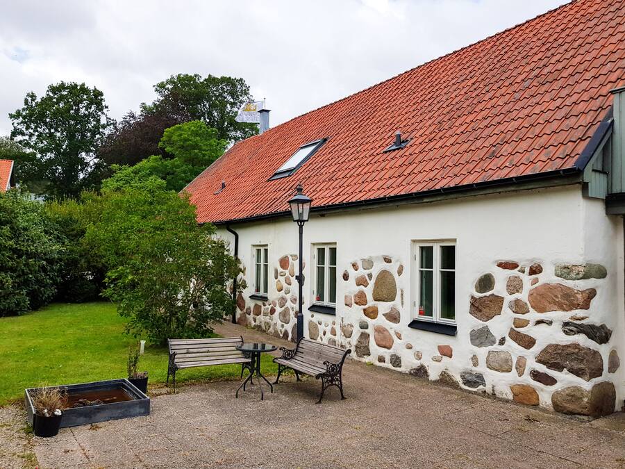 A stone building with a red-tiled roof, a bench, and a small table in the courtyard.