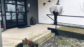 Entrada de un edificio con puerta negra, un pequeño espacio de asientos al aire libre, un farol y una escultura de pájaro en la pared.