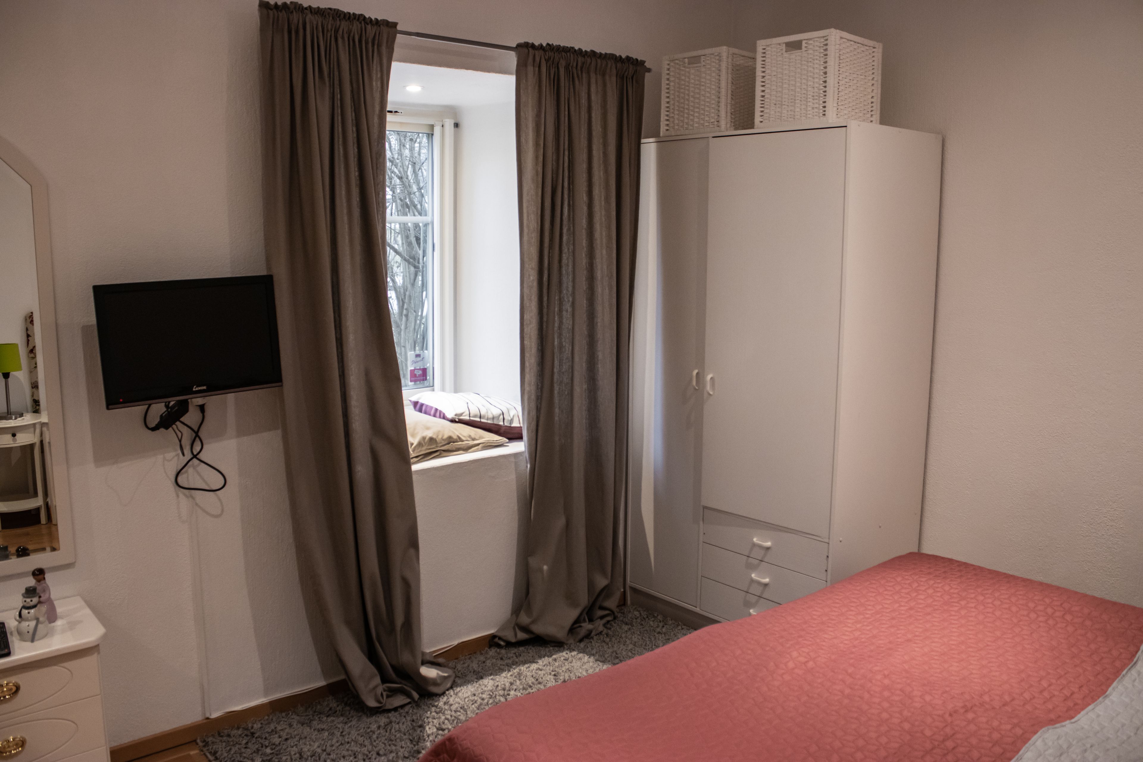 Una camera da letto con un letto, un armadio, una televisione e una finestra con tende.