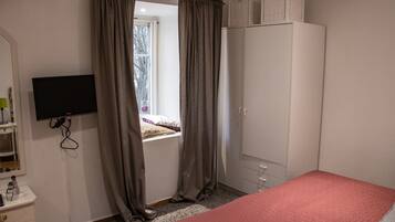 Una camera da letto con un letto, un armadio, una televisione e una finestra con tende.