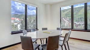 Une salle de conférence dotée d’une table ronde et de six chaises, de grandes fenêtres offrant une vue sur les montagnes et d’un lustre.