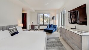Une chambre d’hôtel moderne avec un grand lit, un bureau, un canapé bleu et un téléviseur fixé au mur.