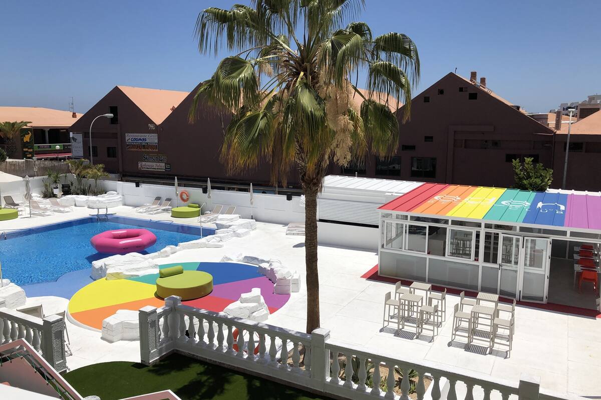 Un área de piscina con un deck colorido, sillas de descanso y una palmera.