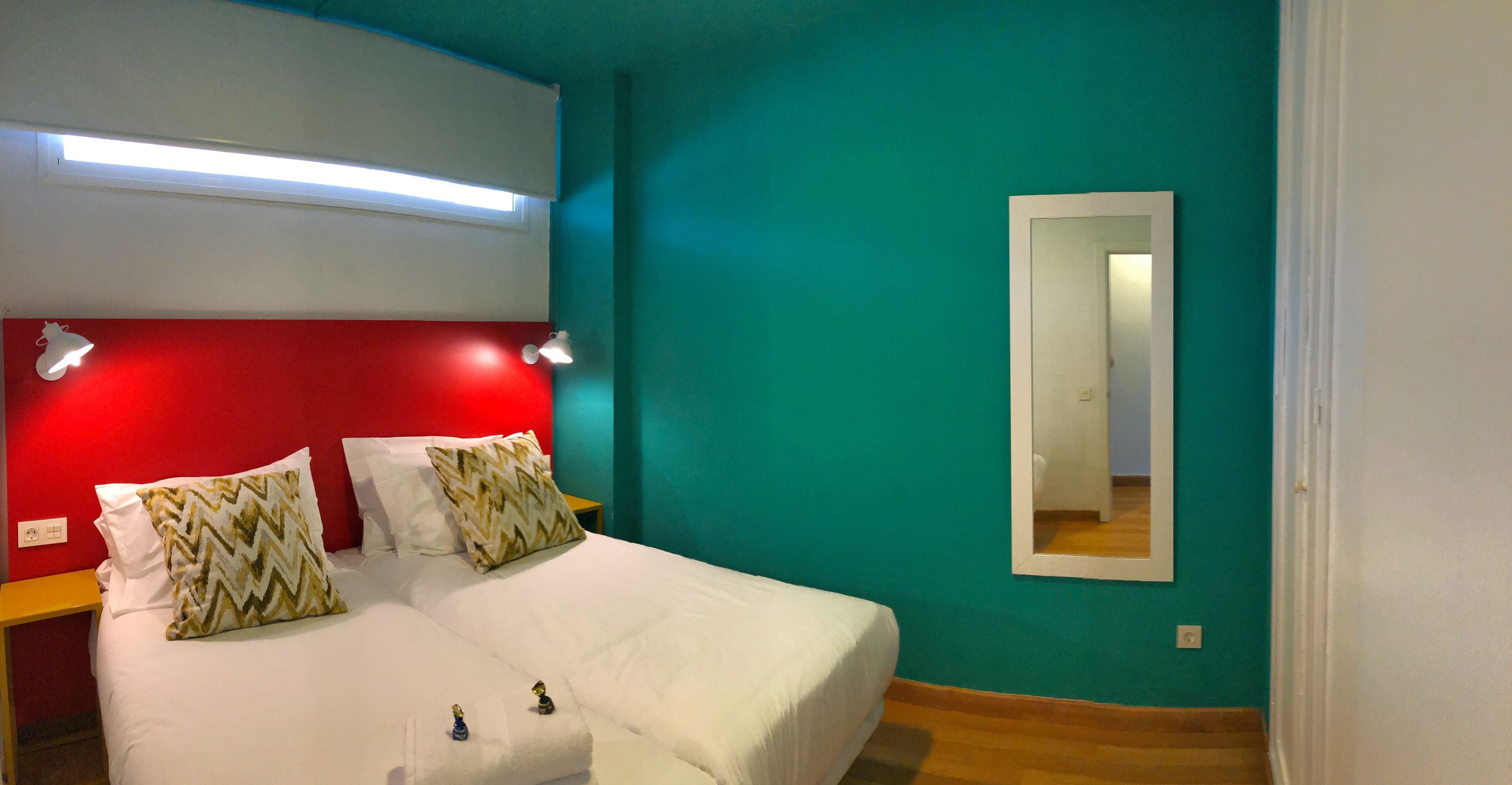 Quarto com cama, mesa de cabeceira, espelho e cabeceira vermelha.