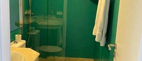 A bathroom with a green wall, a white sink, a toilet, and a shower.