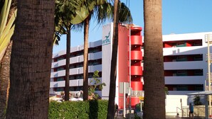 Un immeuble à plusieurs étages, doté d’une façade rouge et blanche, entouré de palmiers.