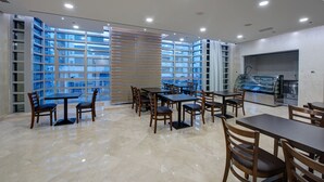 Un espace repas moderne doté de plusieurs tables et chaises, de grandes fenêtres et d’une vitrine.