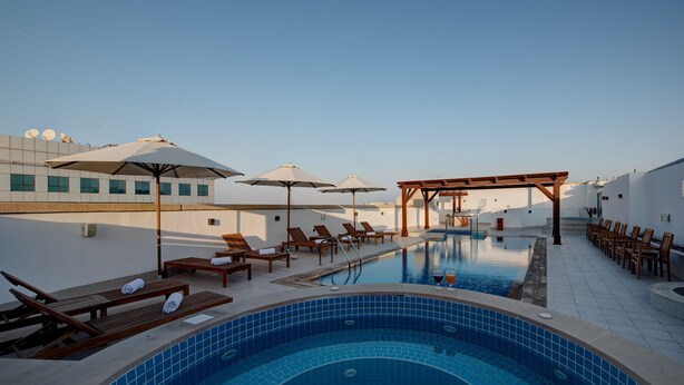 Un espace piscine aménagé sur le toit, avec des chaises longues, des parasols et un jacuzzi.