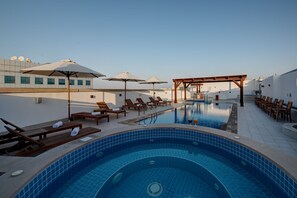 Zona de piscina en la azotea con sillones, sombrillas y una bañera de hidromasaje.