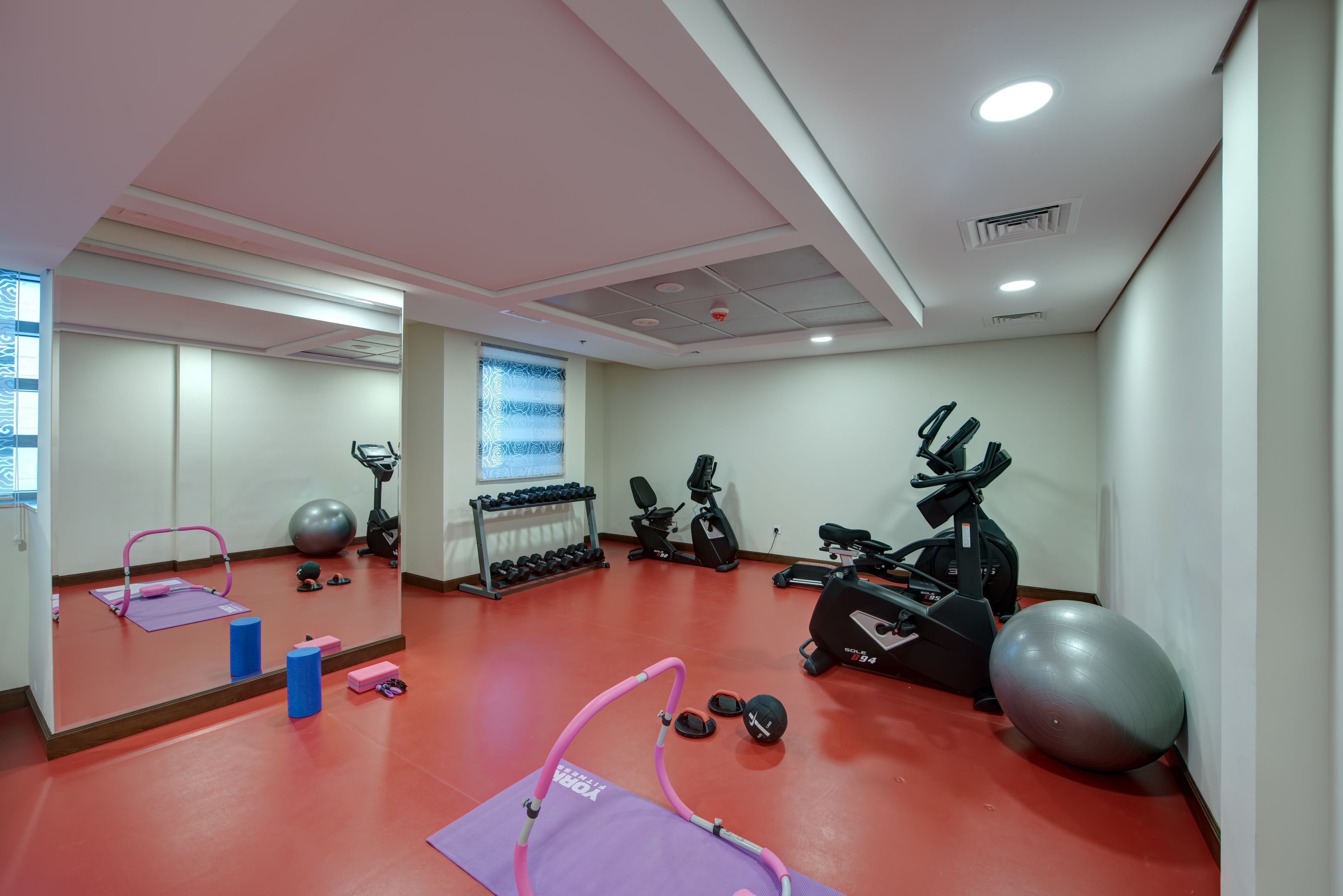 A gym with exercise equipment, a mirror, and a red floor.