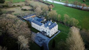 Vista aérea de una extensa propiedad con un edificio principal, un río y campos circundantes.