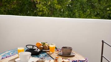 Une table ronde, dressée sur un balcon offrant une vue sur un feuillage verdoyant et luxuriant, est garnie de divers éléments pour le petit-déjeuner, notamment des toasts, des fruits et une théière.
