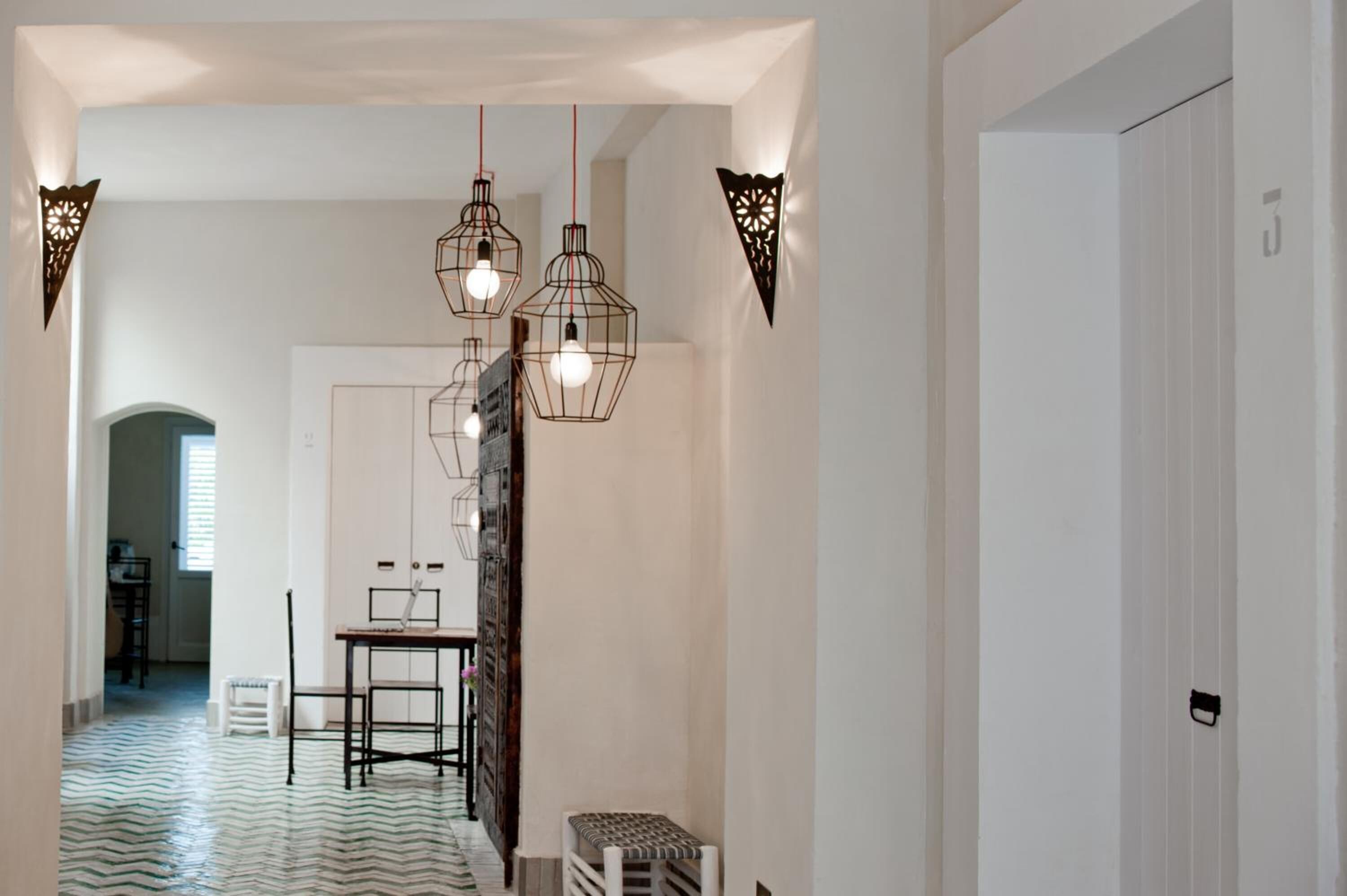 Um corredor com piso estampado, uma mesa e cadeiras, e luminárias pendentes.