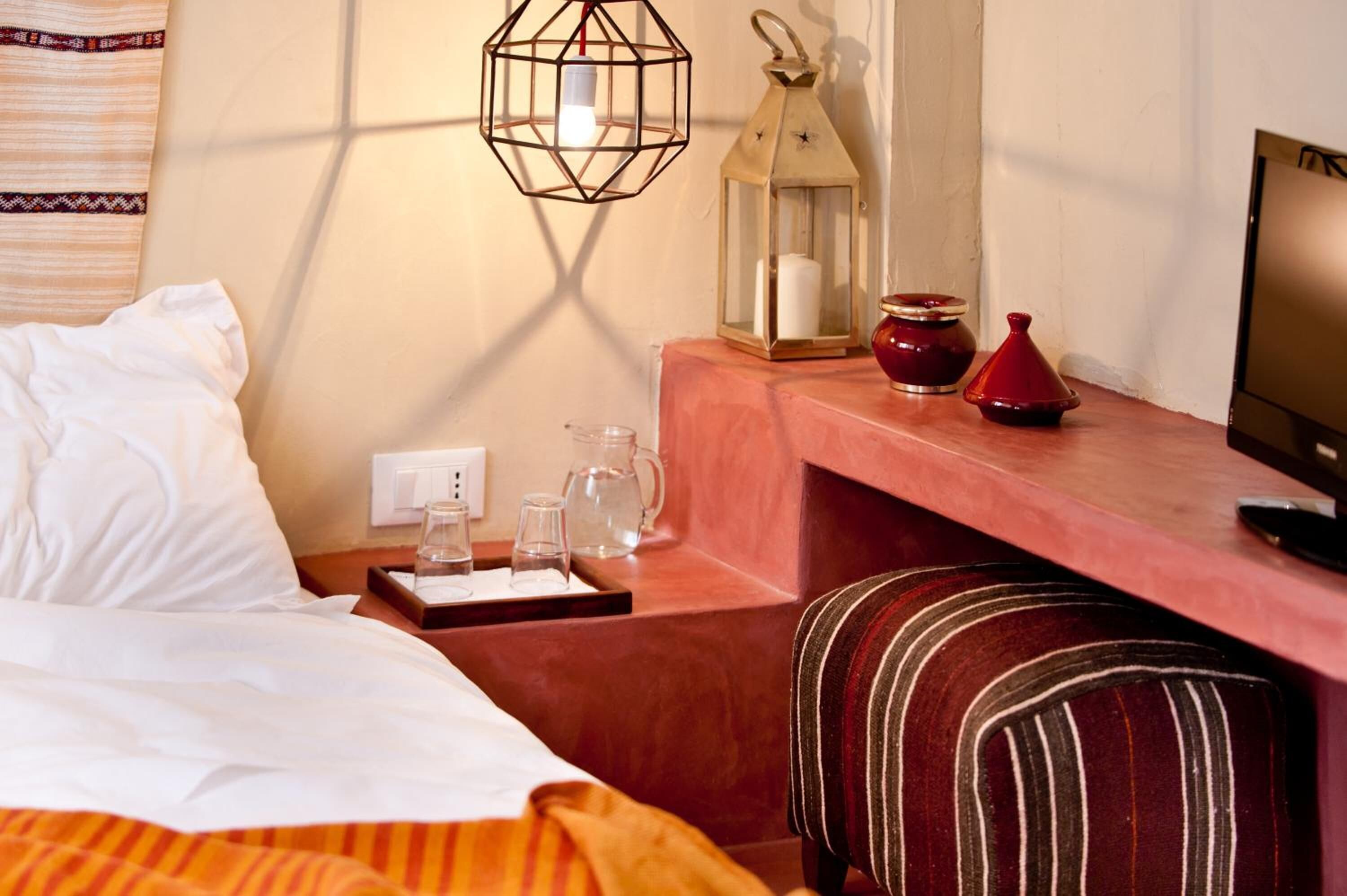 A hotel room with a bed, bedside table with glasses, a lantern, and a TV.
