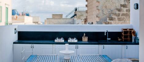 Una terraza en la azotea con mesa y sillas, un mueble blanco y vistas a la ciudad.