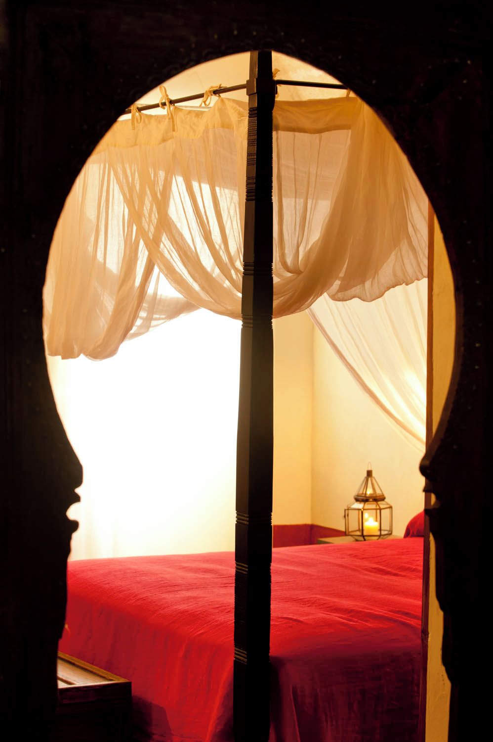 Une chambre avec un lit à baldaquin, une table de chevet et une lanterne.