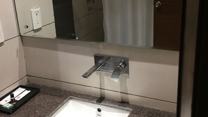 A bathroom with a white sink, a mirror, and a shower visible in the reflection.