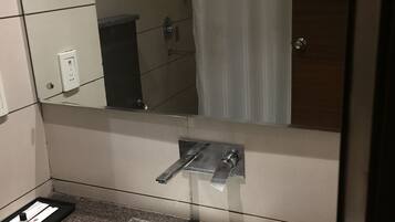 A bathroom with a white sink, a mirror, and a shower visible in the reflection.