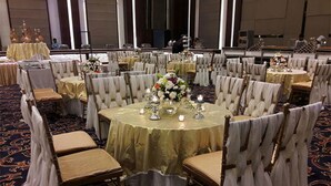 A banquet hall with round tables, white chairs, and floral centerpieces.