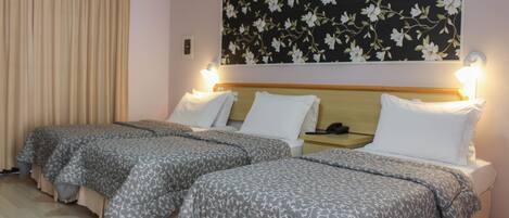 A hotel room with two beds, each with a headboard and bedside tables.