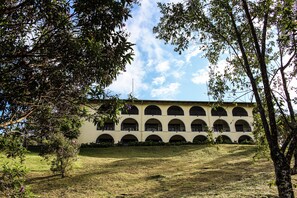 Un edificio con múltiples ventanas de arco y techo plano, rodeado de árboles y césped.